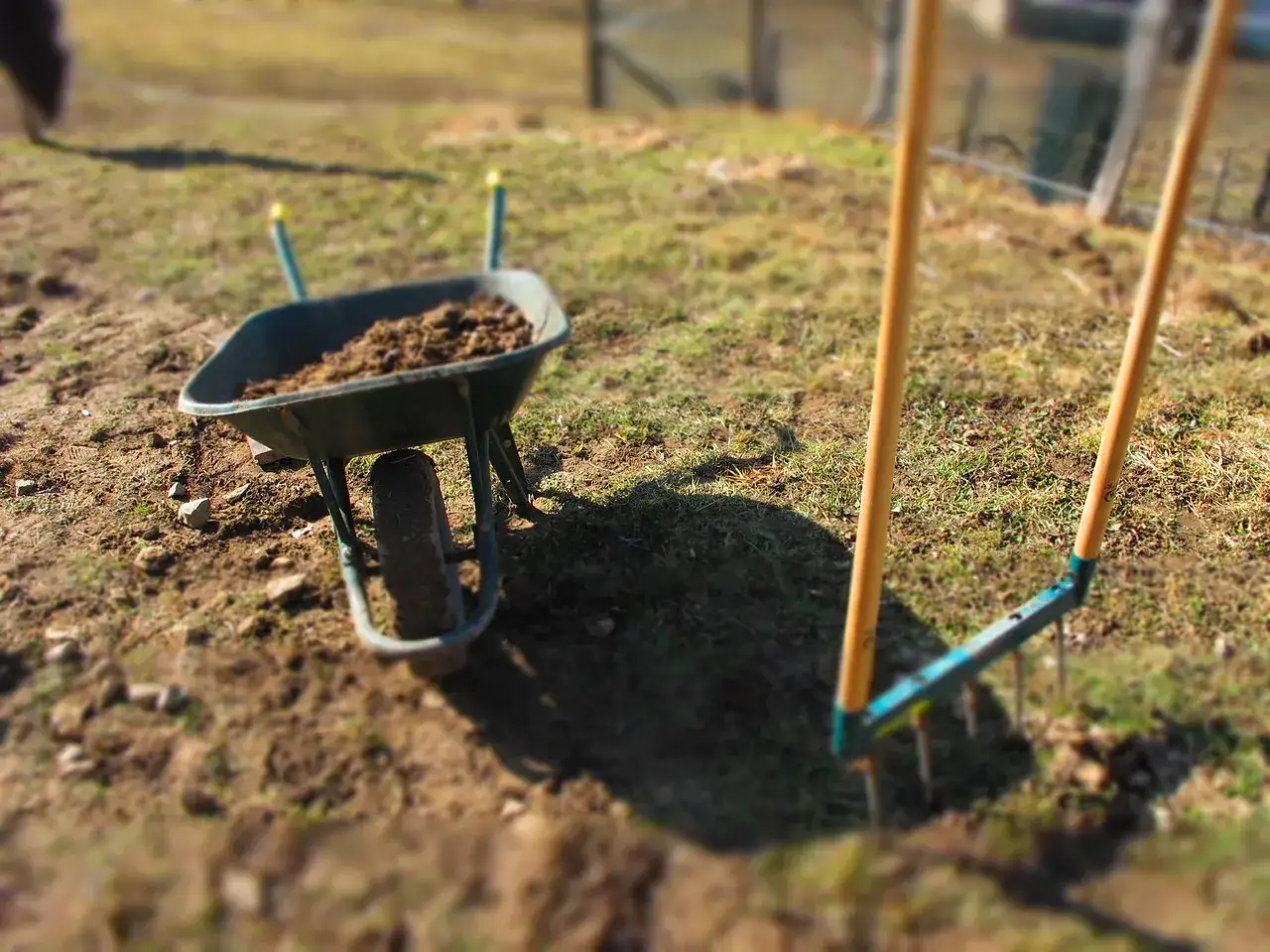 Brouette remplie de terre dure comme de la pierre, &agrave; c&ocirc;t&eacute; d'un r&acirc;teau pr&ecirc;t pour le jardinage.