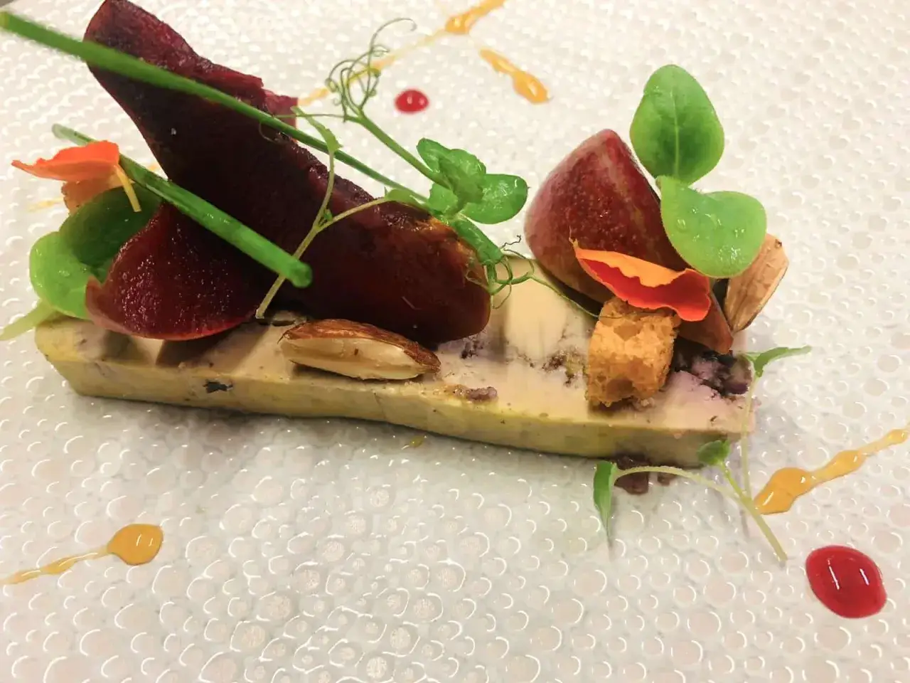 Press&eacute; de foie gras, betterave, amandes et petites pousses vertes, une &oelig;uvre culinaire raffin&eacute;e sur une assiette textur&eacute;e.