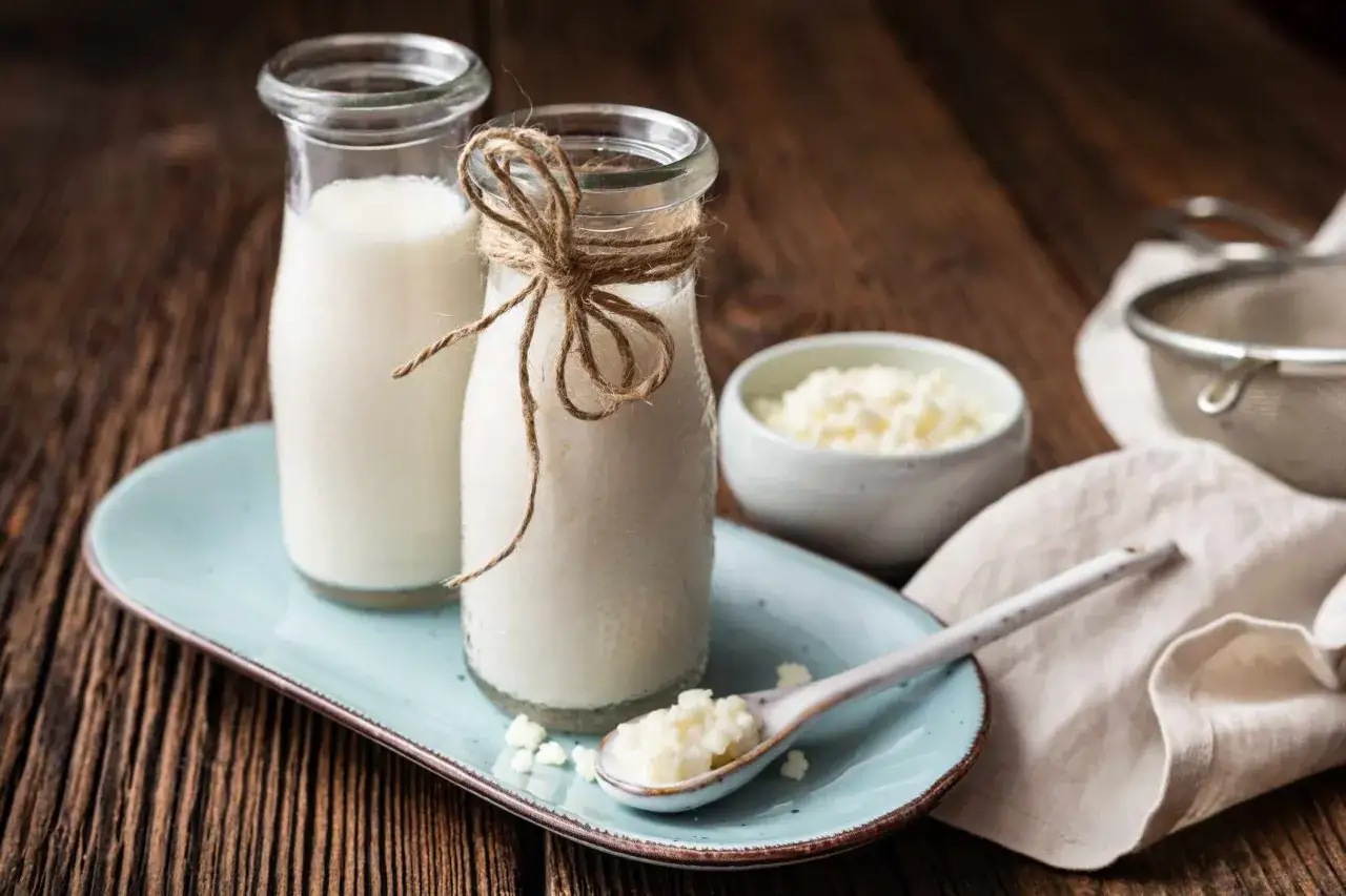 Deux bouteilles de k&eacute;fir de lait, une cuill&egrave;re avec des grains de k&eacute;fir, et un bol de grains. Id&eacute;al pour savoir quand boire du k&eacute;fir.