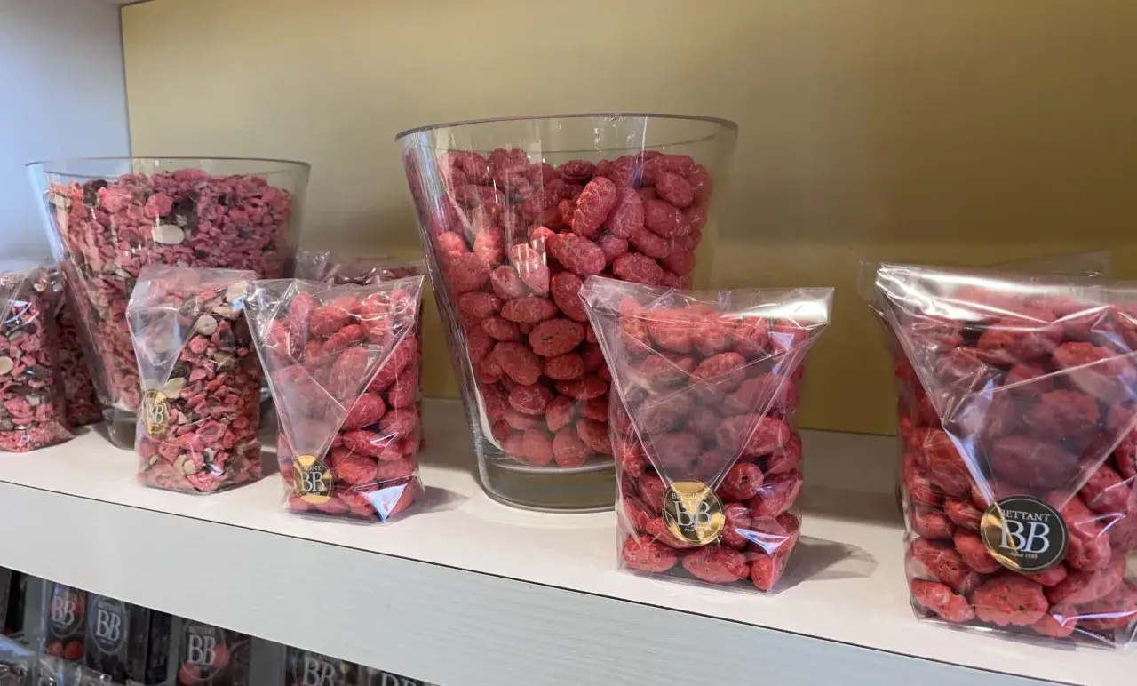 Des bonbons roses, parfaits pour une recette praline rose, sont pr&eacute;sent&eacute;s en vrac dans des bocaux et en sachets sur une &eacute;tag&egrave;re.
