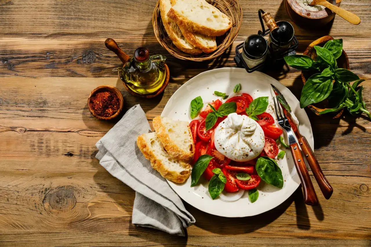 Une assiette de tomates, de basilic et de la burrata cr&eacute;meuse, accompagn&eacute;e de pain croustillant et d'huile d'olive.