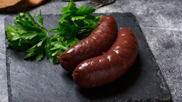Deux boudins rouges antillais, brillants et appétissants, accompagnés de persil frais sur une ardoise sombre.
