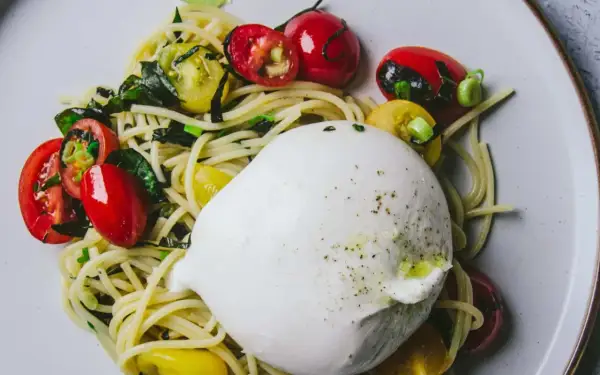 Un plat de pâtes avec une burrata crémeuse, des tomates cerises rouges et jaunes, et des herbes vertes.