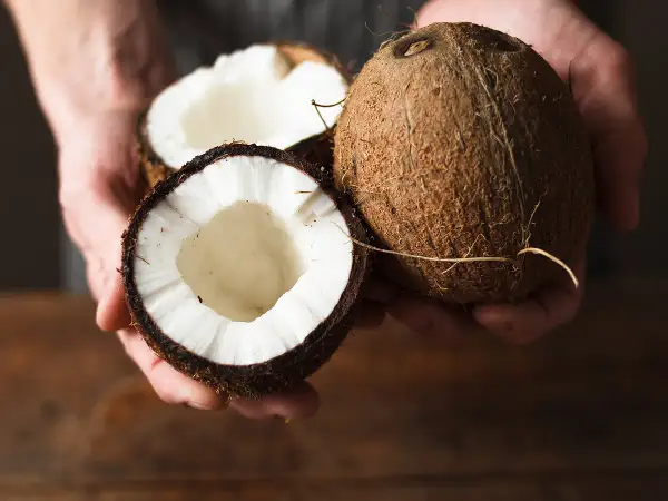Comment choisir une noix de coco : une noix entière et une coupée en deux, révélant sa chair blanche et son eau.