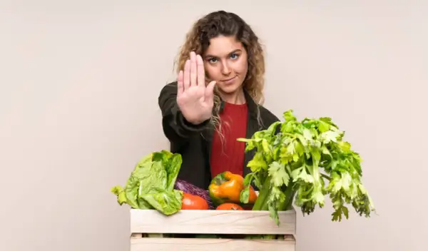 Femme faisant un geste d'arrêt devant une caisse de légumes frais, comme pour dire non aux légumes crus toxiques.