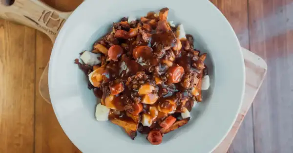 Une assiette généreuse de recette poutine québécoise, avec frites, fromage en grains, sauce brune et morceaux de saucisses.