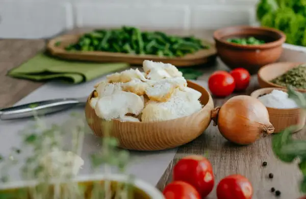 Un bol en bois rempli de champignon criniere de lion, prêt pour une recette savoureuse. Tomates, oignon et herbes l'accompagnent.