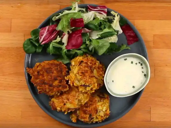 Trois croquettes de légumes dorées, accompagnées d'une salade fraîche et d'une sauce crémeuse.
