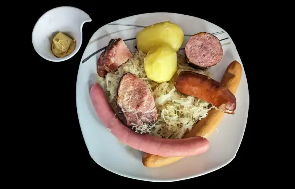 Assiette de choucroute garnie avec pommes de terre, saucisses et viandes, un petit ramequin de moutarde à côté. Un plat riche en saveurs et en vitamine C !